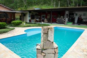 einen Pool mit einer Steinsäule vor einem Haus in der Unterkunft Chácara à beira do lago em São Luiz do Paraítinga in Natividade da Serra