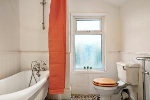 a bathroom with a tub and a toilet and a window at Boutique London Abode - Games Room - Parking in Plumstead