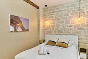 パリにあるResidence Tour Eiffel by Studio prestigeの白いベッドと石の壁が備わるベッドルーム1室
