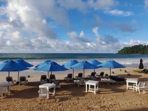 a beach with tables and chairs and blue umbrellas at Brizo Resort in Mirissa