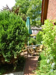 a patio with a table and a green umbrella at Hotel Poggenstool in Neuharlingersiel