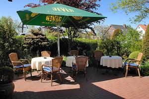 un patio con mesas, sillas y una sombrilla verde en Hotel Poggenstool, en Neuharlingersiel