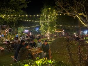 grupa ludzi siedzących przy stolikach w ogrodzie w nocy w obiekcie Hotel Tharu Garden And Beer Bar w mieście Chitwan