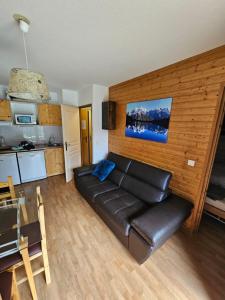 a living room with a leather couch and a kitchen at Les 3 Vallées - Hameau des eaux d'Orelle - Appartement 003 in Orelle