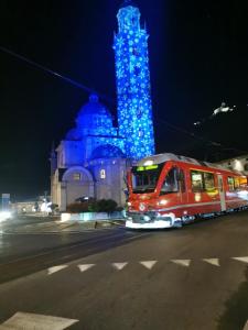 een rode trein die langs een gebouw met een blauwe toren rijdt bij Residenza Le Torri in Tirano