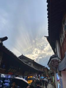 eine Gruppe von Menschen, die mit Sonnenschirmen die Straße hinuntergehen in der Unterkunft Old Town of Lijiang Meiliju Inn in Lijiang