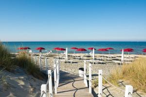 einen Strand mit roten Sonnenschirmen und Stühlen und das Meer in der Unterkunft Acaya Golf Resort & Spa in Acaya