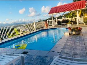 a swimming pool with two chairs and a red roof at Appartement charmant à Rivière-Pilote avec piscine privée in Rivière-Pilote +8 photos
