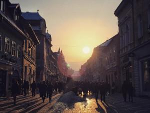 a group of people walking down a street at sunset at BrasovApart Republicii in Braşov