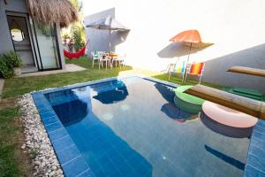 een zwembad met stoelen en een parasol naast een huis bij Casa Milagres 03 suítes - 300m da Praia, 6 pessoas in Pôrto de Pedras