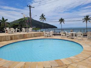 una piscina con mesas y sillas y el océano en Maravilhoso apto à beira-mar, en Caraguatatuba