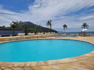 uma grande piscina azul com cadeiras e o oceano em Maravilhoso apto à beira-mar em Caraguatatuba