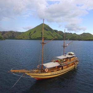 a boat in the water with a mountain in the background at Phinisi Floresta Komodo in Labuan Bajo