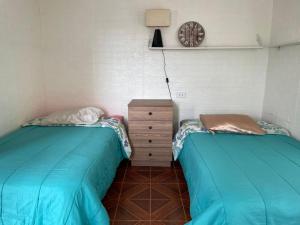 two beds in a room with a dresser and a clock at Casita acogedora en cusco in Cusco