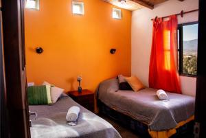 2 camas en una habitación con paredes de color naranja y ventana en Cabaña Paraíso Cachi en Cachí