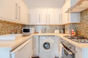 a kitchen with white cabinets and a washer at Radiant and Roomy 2BD Flat - Fulham! in London