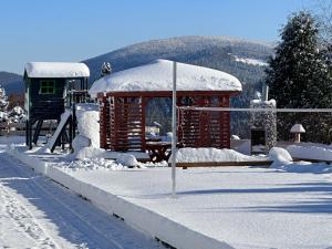 een klein gebouw in de sneeuw met een speeltuin bij Domek drewniany w górach Jacuzzi & Balia - Osada Chełm in Stróża