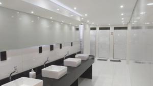 a white bathroom with four sinks and stalls at Hotel Dalcol Economic in Telêmaco Borba