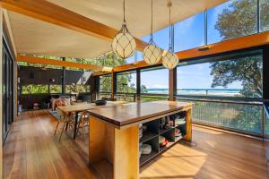 an open kitchen with large windows and a dining table at Kawakawa House - Piha Holiday Home in Auckland