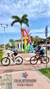 two people riding bikes on a sidewalk in a city at Hotel Familiar El Dorado in Zihuatanejo