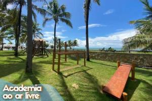 un parque con un banco, palmeras y el océano en Itacimirim Villas da Praia en Camassari