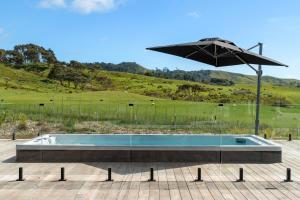 a swimming pool with an umbrella next to a field at Te Karaka Lodge in Port Waikato