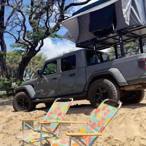 twee stoelen en een jeep geparkeerd in het zand bij Embark on a journey through Maui with Aloha Glamp's jeep and rooftop tent allows you to discover diverse campgrounds, unveiling the island's beauty from unique perspectives each day in Paia