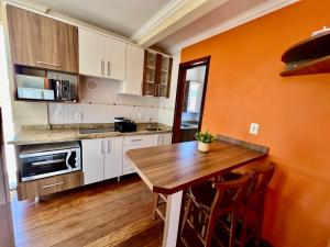 eine Küche mit einer orangefarbenen Wand und einem Holztisch in der Unterkunft Acorde Com o Cenário Beira Mar - Coberturinha in Bombinhas