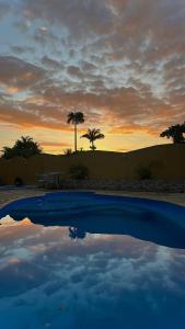 a sunset over a pool with a table and palm trees at Pousada Bosque dos Papagaios in Búzios