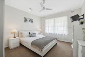 um quarto branco com uma cama e uma ventoinha de tecto em Belle Escapes - Vitamin Sea at Henley Beach em Henley Beach South