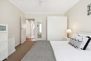 a white bedroom with a bed and a dresser at Belle Escapes - Vitamin Sea at Henley Beach in Henley Beach