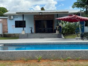 D'Camp Homestay with swimming pool في Kampong Kenangan: منزل به مسبح ومظلة حمراء