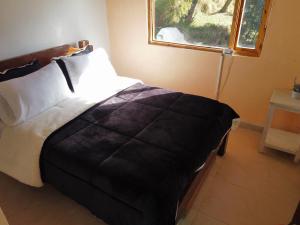 a bedroom with a bed with a black blanket and a window at Rancho New Life Guatavita in Guatavita