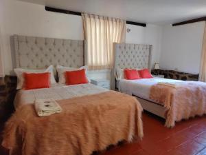 a bedroom with two beds with orange pillows at Hotel Casablanca in Ollantaytambo