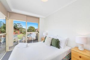 a white bedroom with a bed and a balcony at Seaspray Unit 3 4 Intrepid Close in Nelson Bay