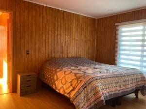 a bedroom with a bed with wooden walls and a window at Cabañas Las Márgaras Uno in Llanquihue