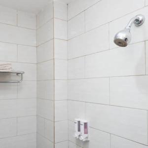 una doccia piastrellata di bianco con luce sul muro di Capital Hotel Makassar a Pampang