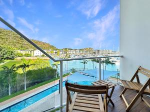 a balcony with two chairs and a table and a pool at Waterfront Townhouse 'Beachside Apartment 16' - Central location, pool, good wifi in Nelly Bay