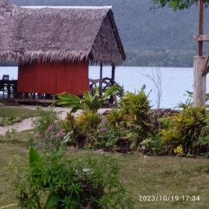 a house with a thatched roof next to the water at Serenity Bungalows in Port Olry