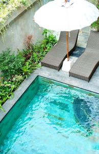 a swimming pool with an umbrella and two chairs at Santera Village in Canggu
