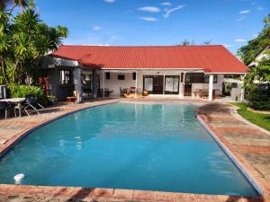 a swimming pool in front of a house with a red roof at Mukala Lodge in Lusaka