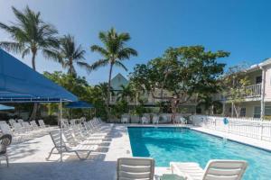 una piscina con sillas blancas y una sombrilla azul en Lavender Jungle by AvantStay Great Location w Patio Shared Pool Week Long Stays Only, en Key West