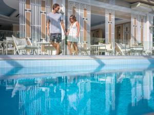 a man and woman standing next to a swimming pool at Secret Paradise Hotel & Spa in Nea Kallikrateia