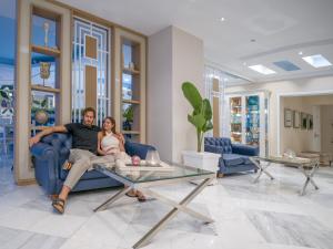 a man and woman sitting on a couch in a living room at Secret Paradise Hotel & Spa in Nea Kalikratia