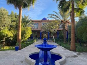 une fontaine bleue devant un bâtiment planté de palmiers dans l'établissement Hotel L'Oliveraie Jnane Zitoune, à Marrakech