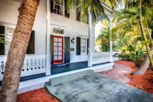 a white house with a red door and palm trees at Casa de Rosalie by AvantStay Great Location w Pool BBQ Outdoor Dining Month Long Stays Only in Key West