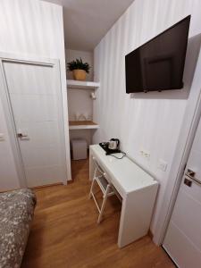Habitación pequeña con escritorio blanco y TV en la pared. en Hostal A Nuestra Senora de La Paloma en Madrid