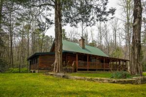 une cabane en rondins avec un toit vert dans les bois dans l'établissement Twin Creeks Lodge by AvantStay 33 Acre Retreat, à Brevard