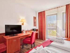 Zimmer mit einem Schreibtisch, einem TV und einem Bett in der Unterkunft Mercure Hotel Bad Duerkheim An Den Salinen in Bad Dürkheim