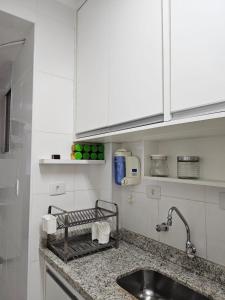 um balcão de cozinha com um lavatório e armários brancos em Apartamentos na Praia do Gonzaga em Santos